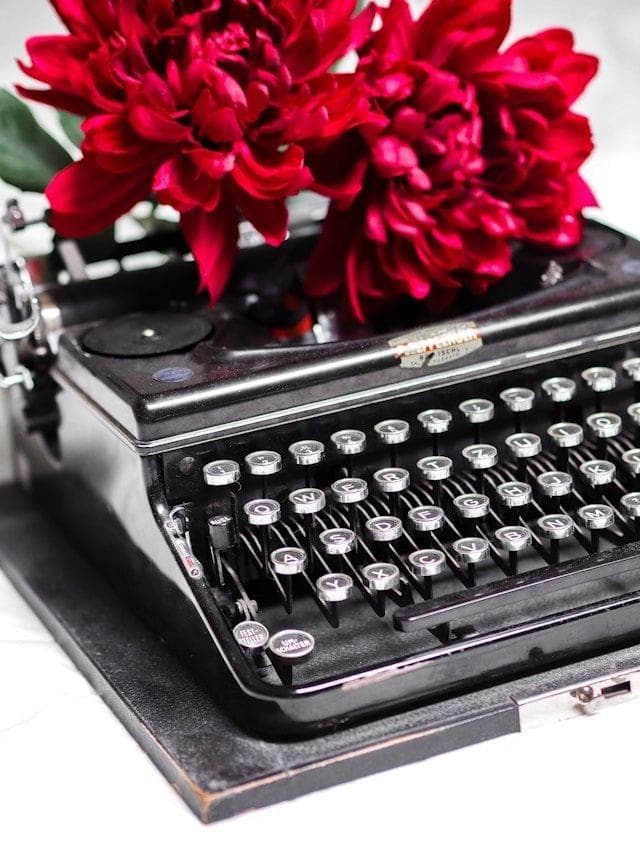 black typewriter with red flowers on top of it