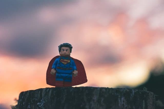lego superman standing on a stump with a bokeh sunset behind him